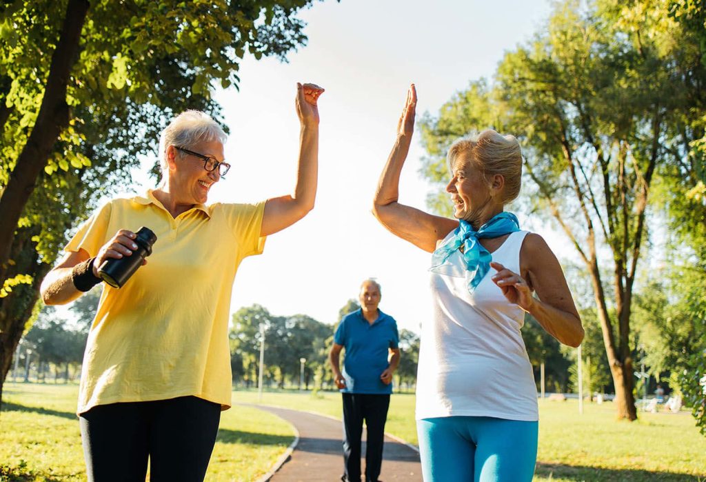 Two senior women high-fiving in bright activewear during outdoor workout in sunlit park background Wallpaper