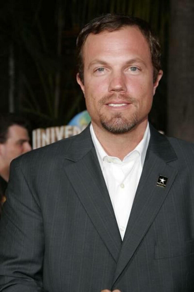 Actor Adam Baldwin in dark suit posing confidently at event wallpaper background
