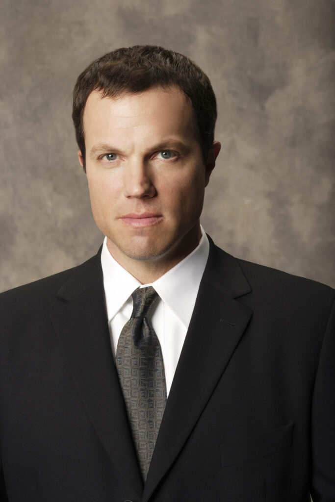 Adam Baldwin formal portrait wearing black suit and patterned tie against neutral backdrop Wallpaper