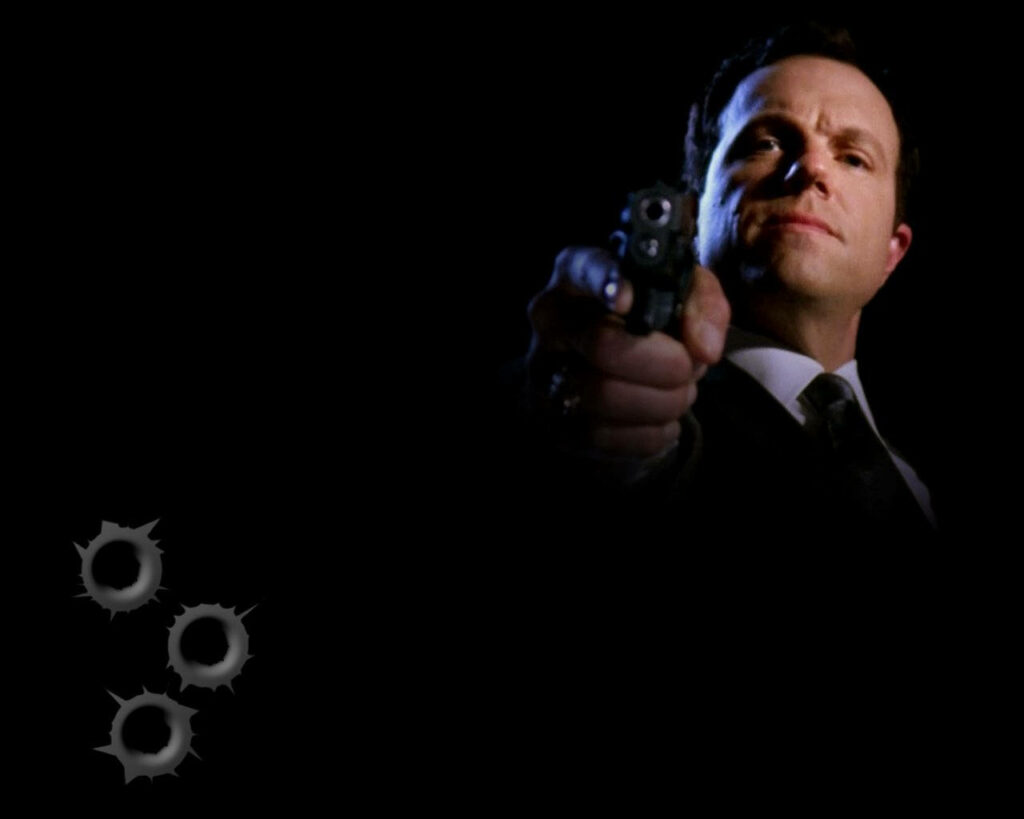 Adam Baldwin pointing gun with three gunshot holes dark intense action wallpaper background