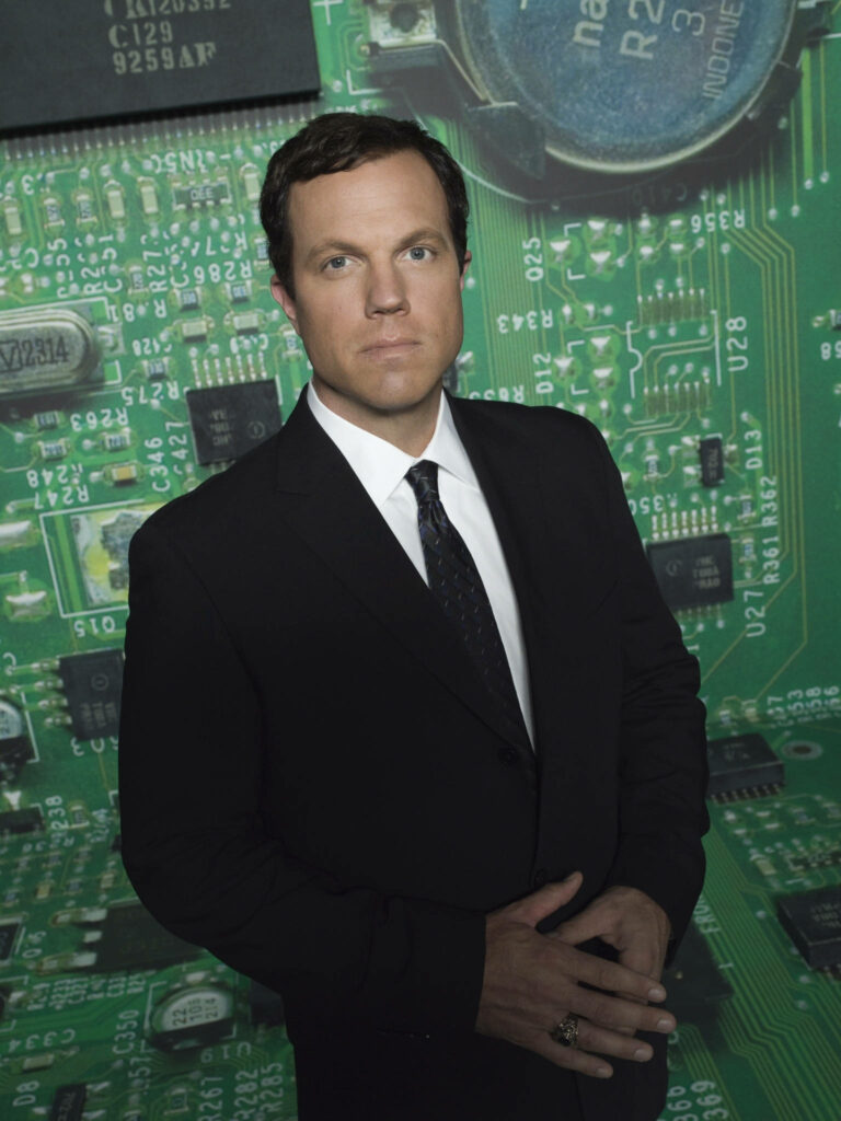 Adam Baldwin in suit with vibrant circuit board background technology professional wallpaper
