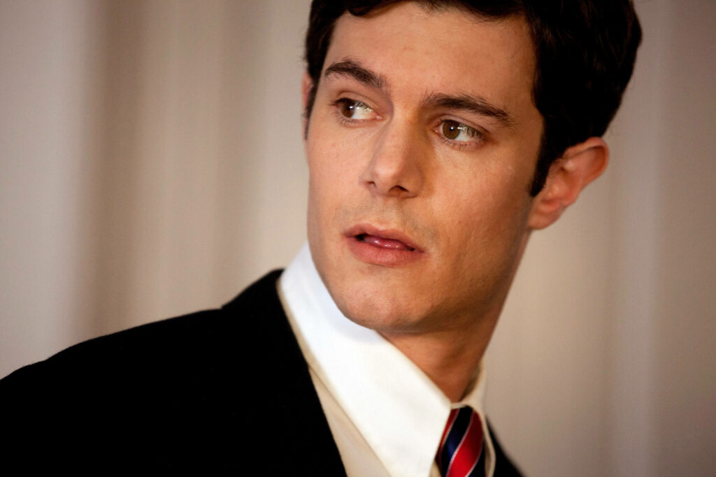 Adam Brody in black suit and striped tie classic portrait with soft blurred wallpaper background