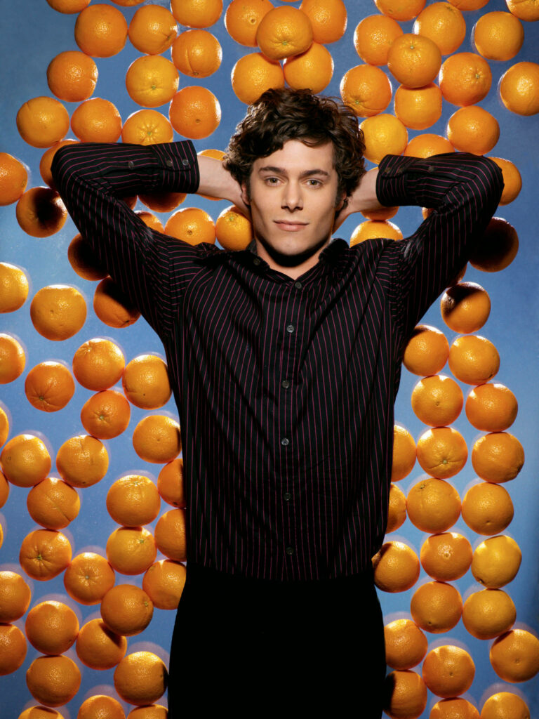 Adam Brody posing confidently with floating oranges colorful vibrant playful wallpaper background