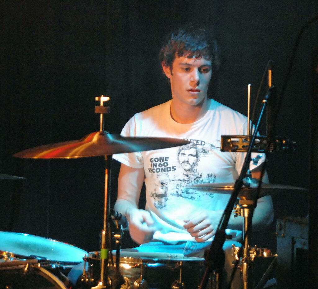 Adam Brody focused playing drums behind drum kit vibrant music wallpaper background for fans