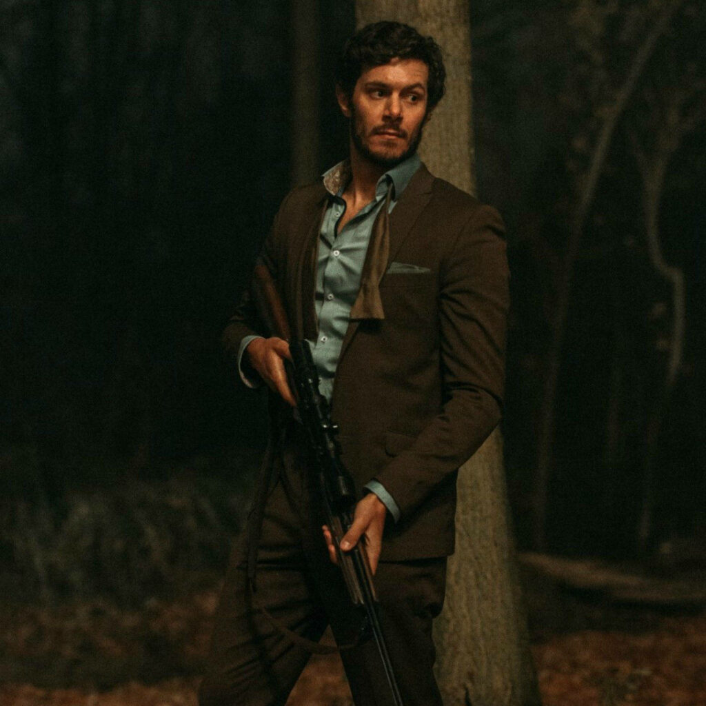 Adam Brody in suit holding shotgun in dark forest at night suspenseful intense wallpaper background