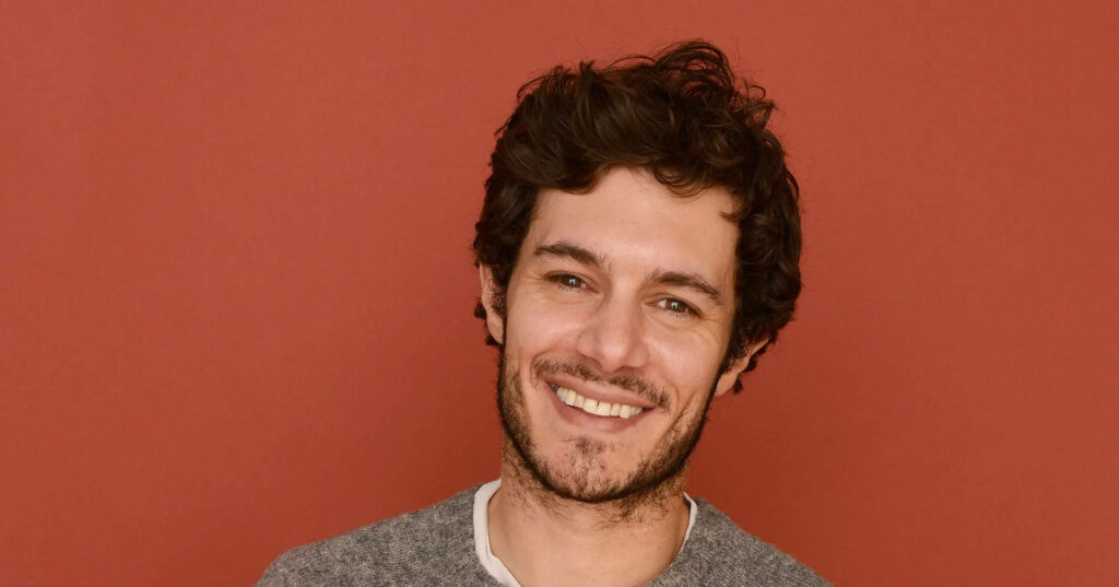 Adam Brody smiling warmly against a plain red background cheerful inviting wallpaper image