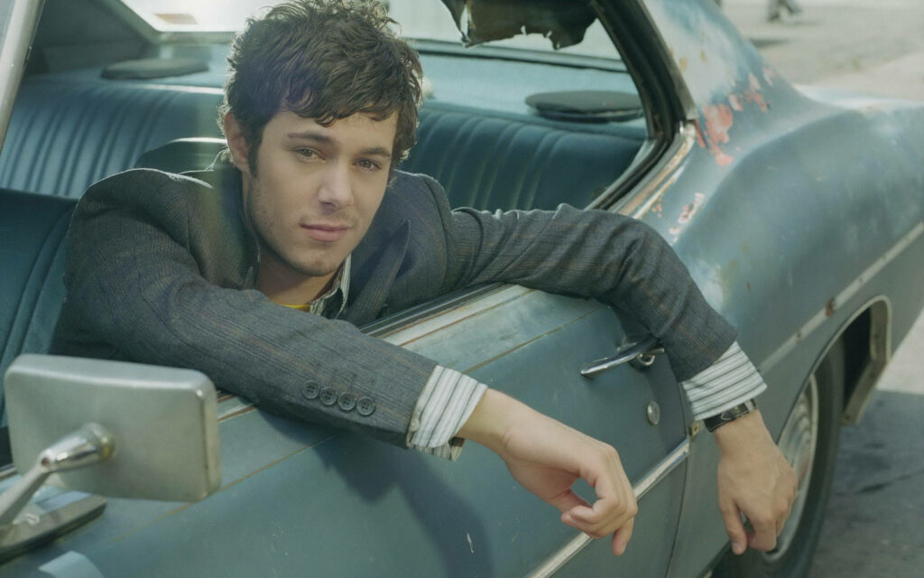 Adam Brody in vintage car driver seat creating nostalgic cool atmosphere wallpaper background