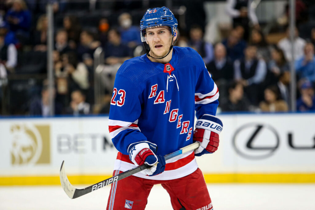 Adam Fox in blue New York Rangers jersey focused on ice during intense hockey game action Wallpaper