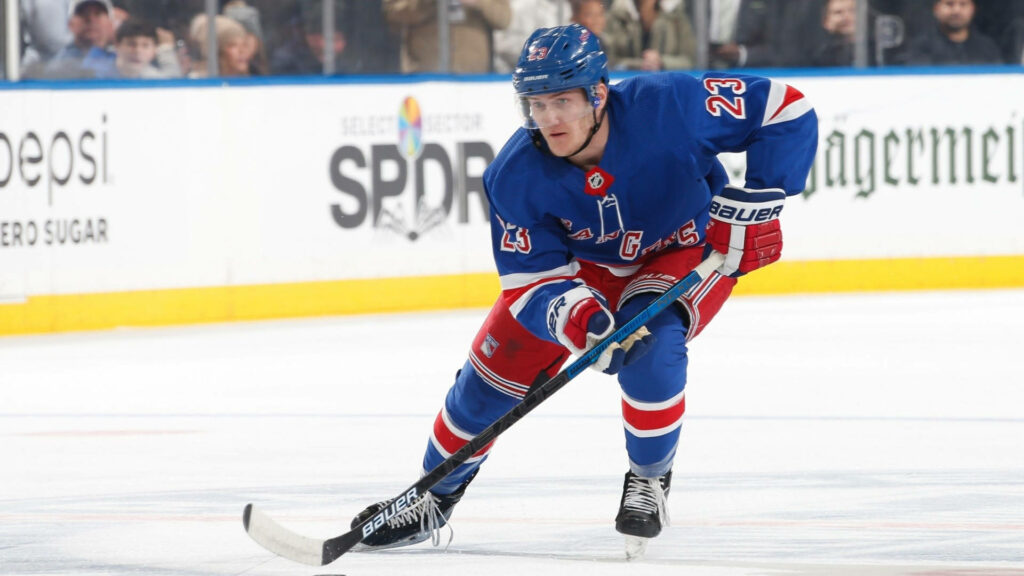 Adam Fox in blue New York Rangers uniform skating with focus and agility on ice hockey wallpaper