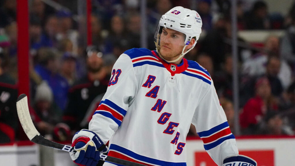 Adam Fox focused in New York Rangers white jersey standing on ice during intense hockey game Wallpaper