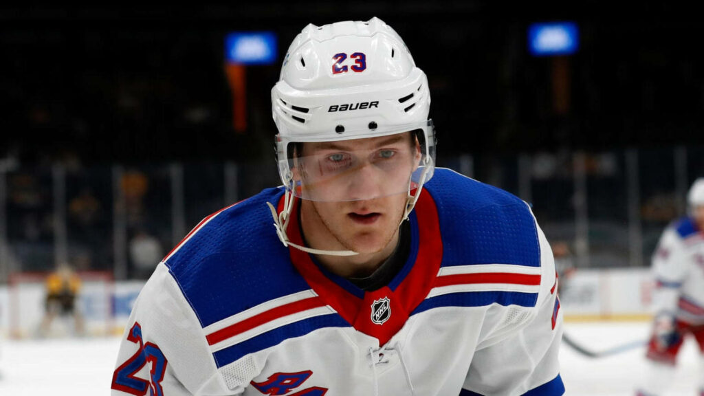 Adam Fox focused in white New York Rangers jersey and helmet on intense hockey rink background Wallpaper