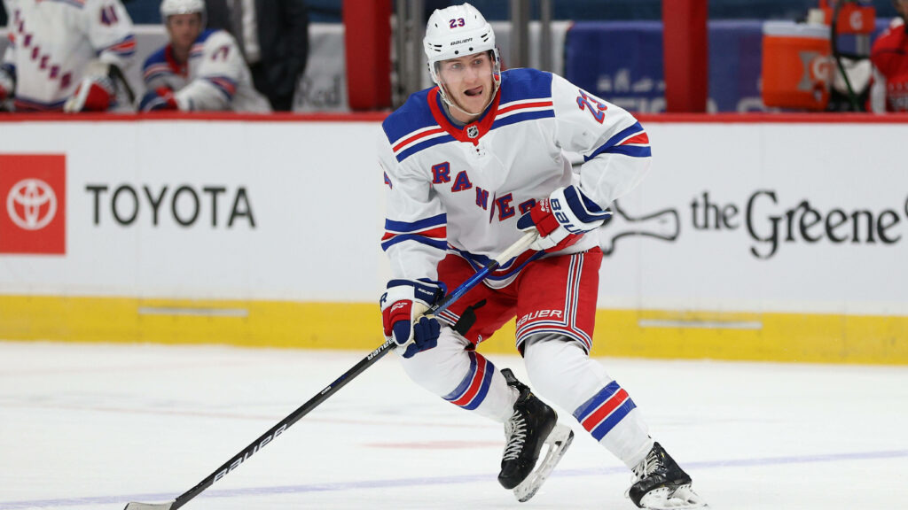 Adam Fox New York Rangers in white uniform skating focused during intense hockey game Wallpaper