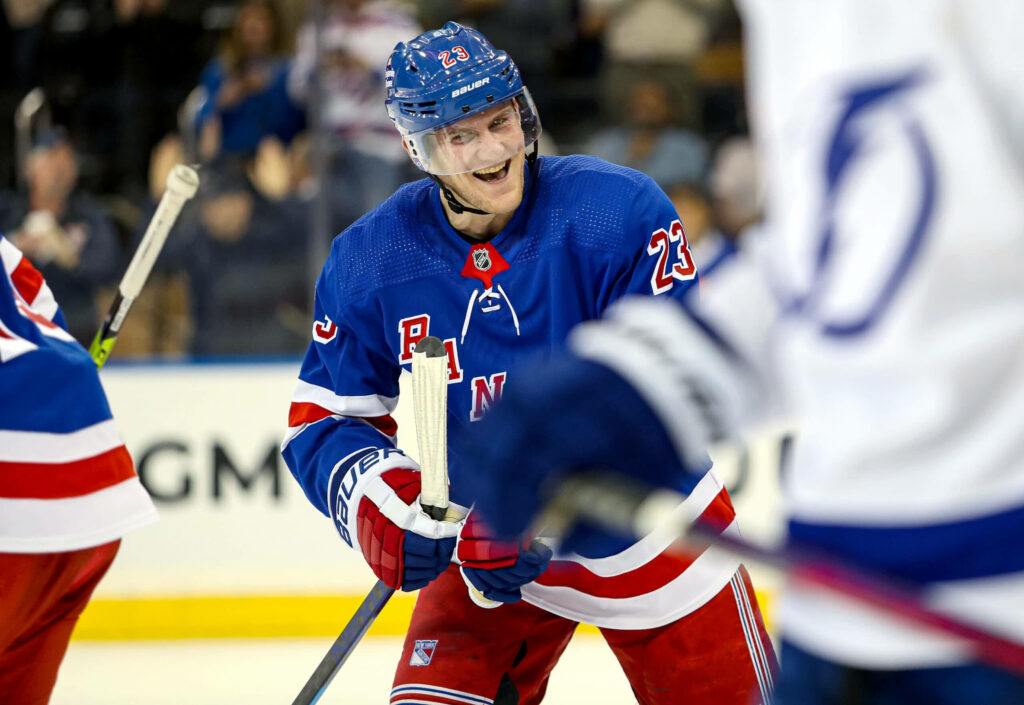 Adam Fox smiling on ice wearing New York Rangers jersey NHL player wallpaper background