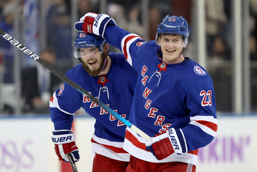Adam Fox and Ryan Lindgren celebrate on ice in New York Rangers uniforms during hockey game Wallpaper