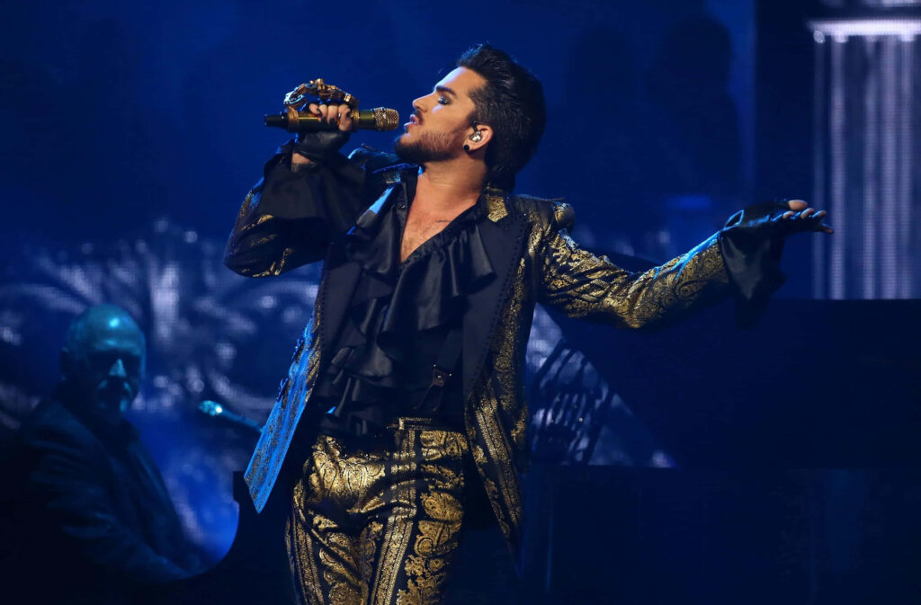 Adam Lambert singing live in gold suit under blue stage lights vibrant concert performance wallpaper