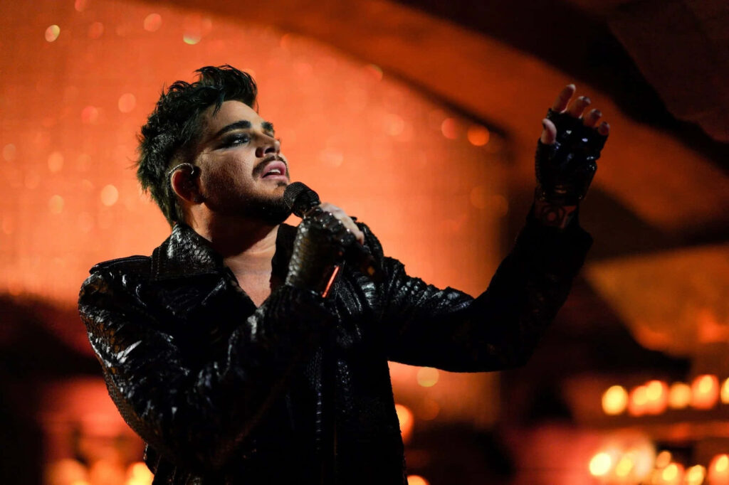 Adam Lambert performing live in black leather outfit with dramatic makeup and warm stage lights Wallpaper