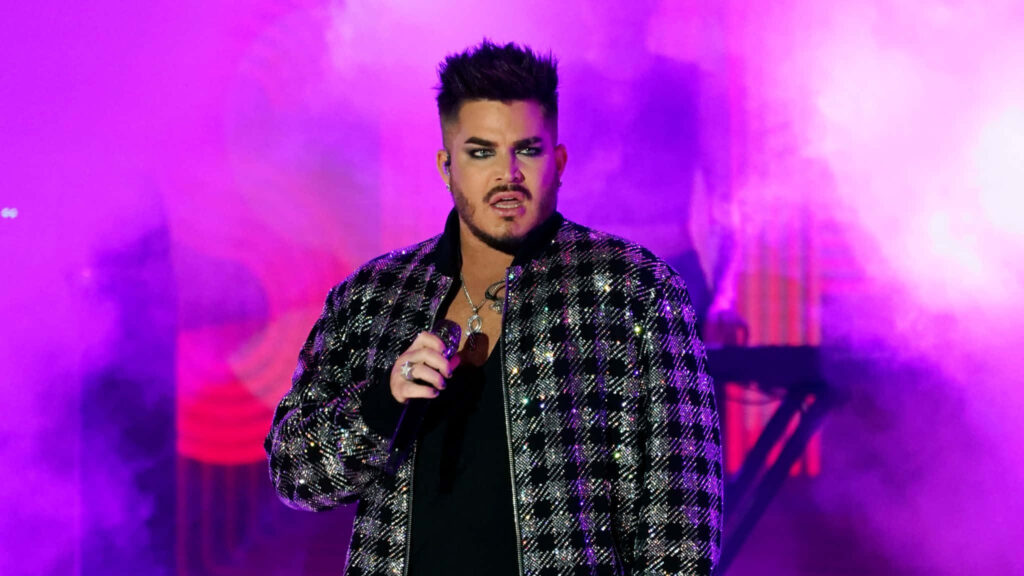 Adam Lambert singing on stage in patterned jacket with vibrant purple pink lights background Wallpaper