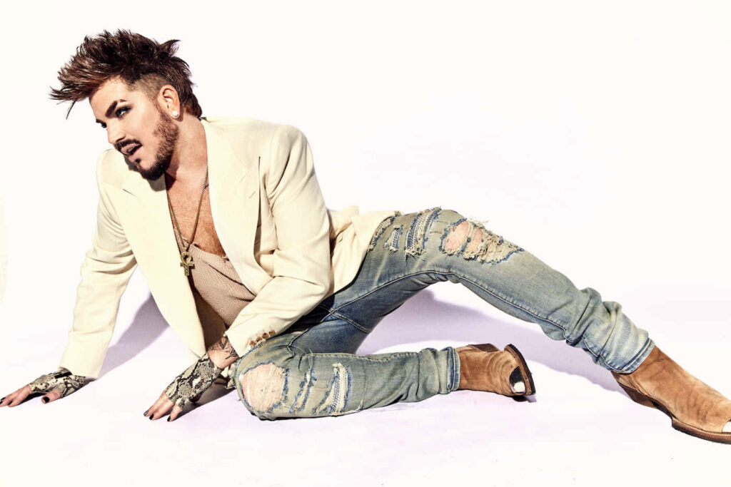 Adam Lambert stylish in cream blazer ripped jeans tan boots bright white background fashion pose Wallpaper