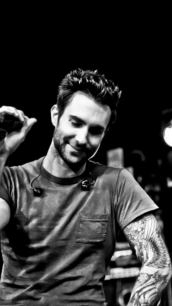 Greyscale portrait of Adam Levine with tattoos, casual style, and a captivating live performance vibe. Wallpaper