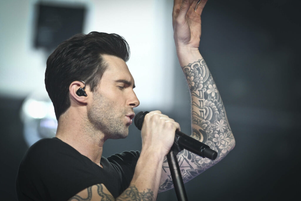 Adam Levine performing live with microphone, showcasing tattoos and stylish energy as wallpaper.