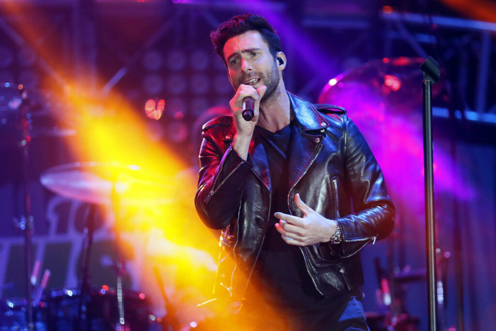 Adam Levine showcases style in a black leather jacket on stage with vibrant lighting. Wallpaper