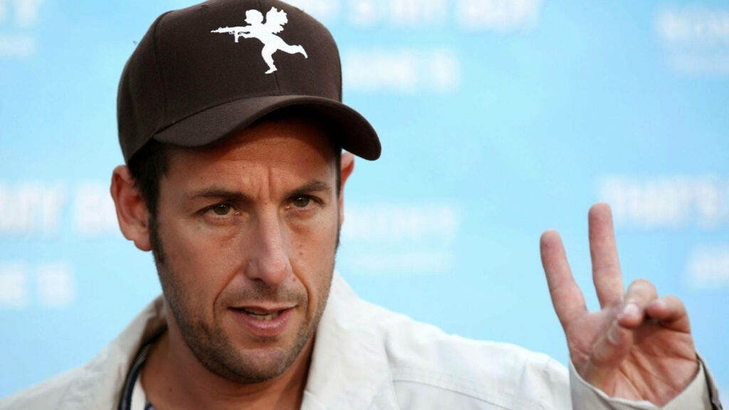 American comedian Adam Sandler giving peace sign wearing brown cap with playful graphic on blue background Wallpaper
