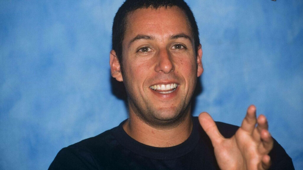 Adam Sandler smiling brightly against blue background lively expression wallpaper image