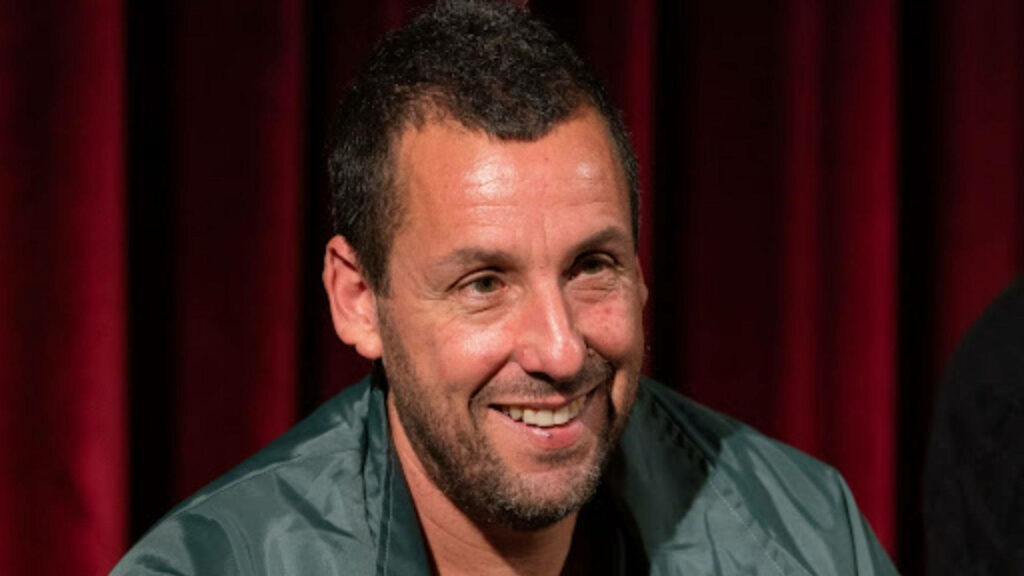 Adam Sandler smiling brightly against warm red curtain background wallpaper radiating charm