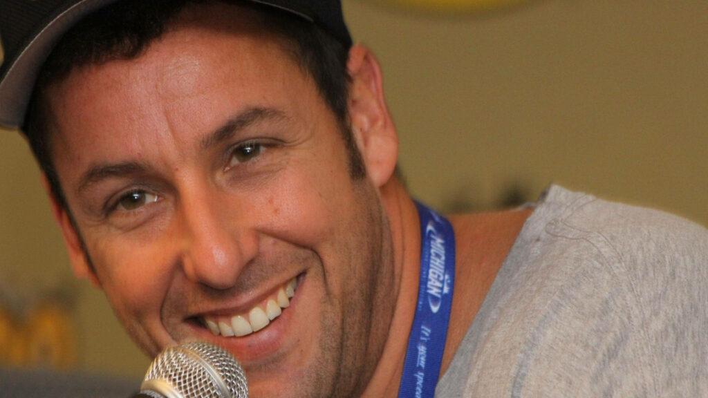 Adam Sandler smiling warmly speaking into microphone lively friendly wallpaper background