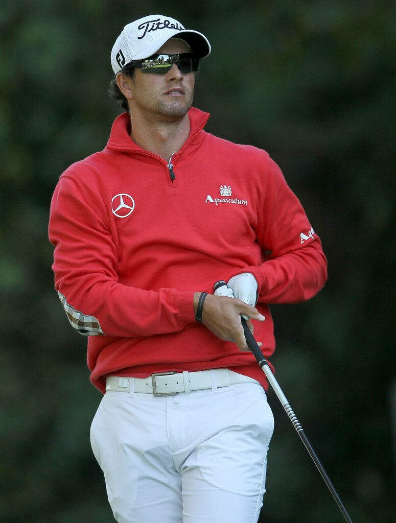 Adam Scott in red jacket and white cap focused preparing golf swing on course wallpaper background
