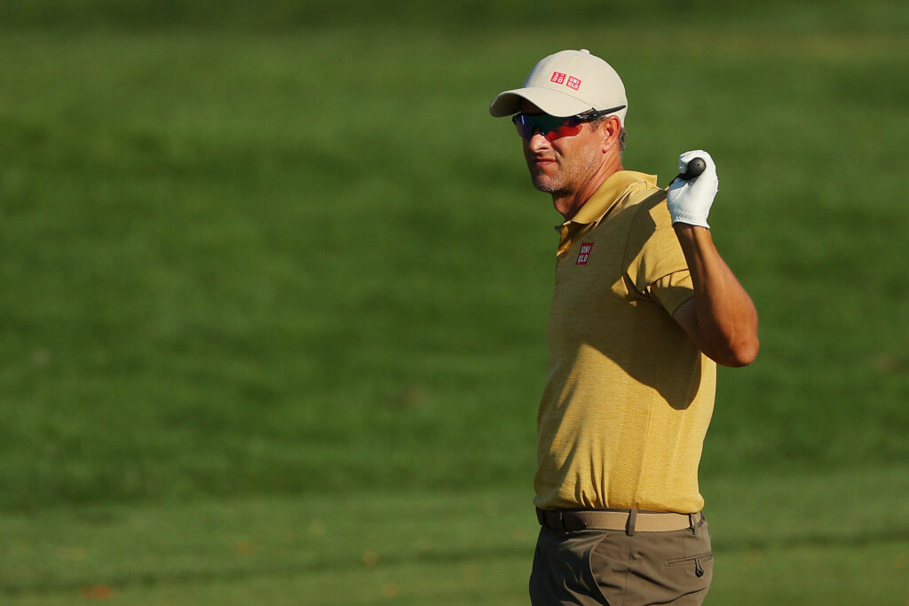 Adam Scott golfer in yellow shirt and beige cap on lush green golf course holding club over shoulder Wallpaper