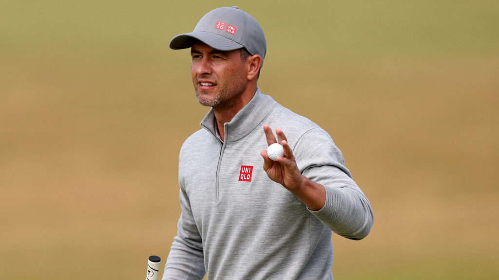 Adam Scott holding golf ball on course wearing grey jacket and cap dynamic golf wallpaper background