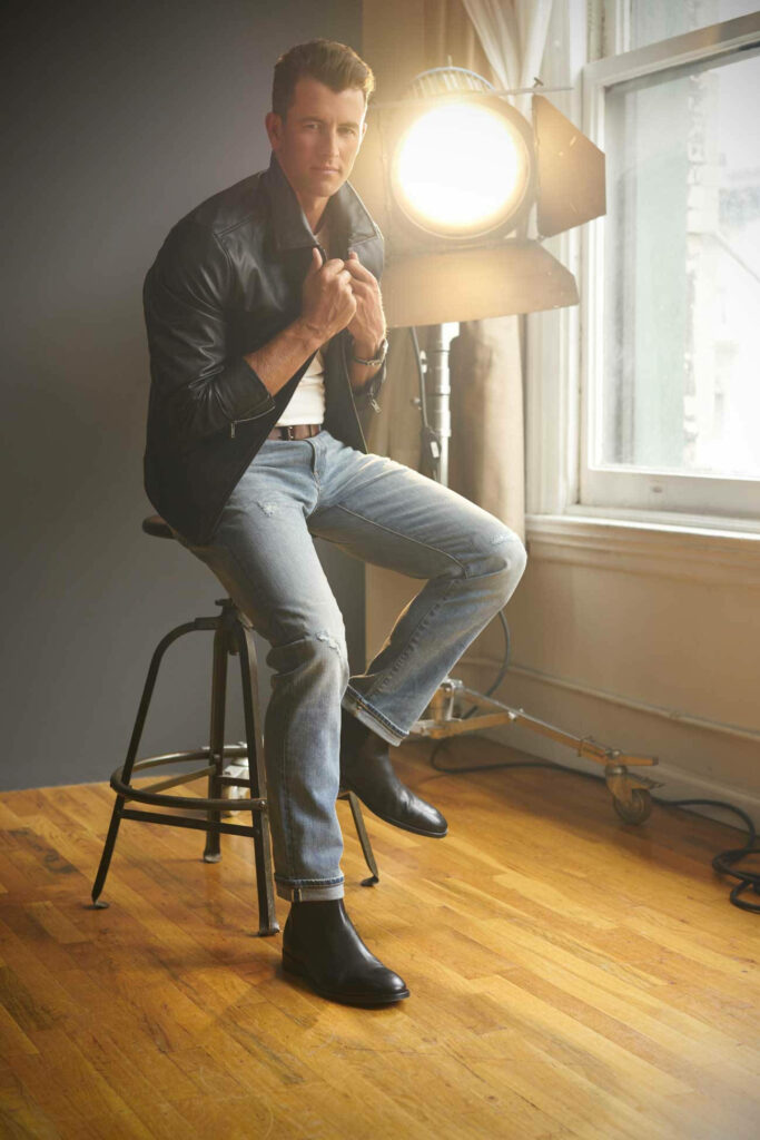 Adam Scott in leather jacket sitting on stool with bright studio light sleek modern background Wallpaper