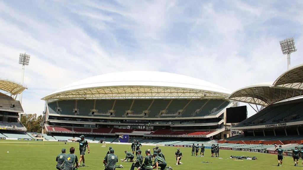 Cricket practice session at Adelaide Oval with players on green field and stadium architecture Wallpaper