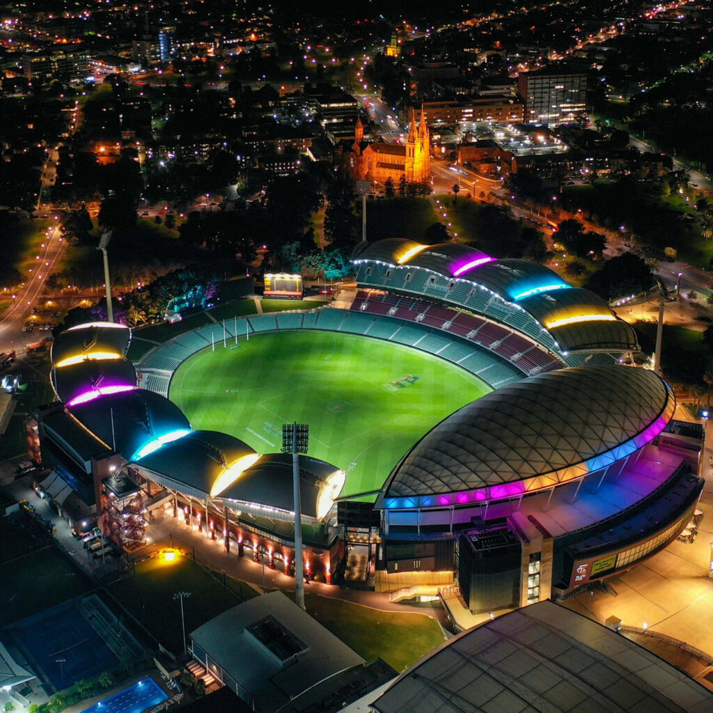 Aerial night view of Adelaide Oval illuminated with vibrant lights and city skyline background Wallpaper