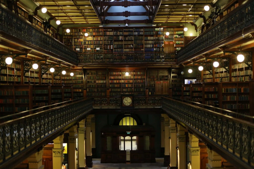 Interior of Adelaide State Library with ornate railings towering bookshelves and classic clock Wallpaper