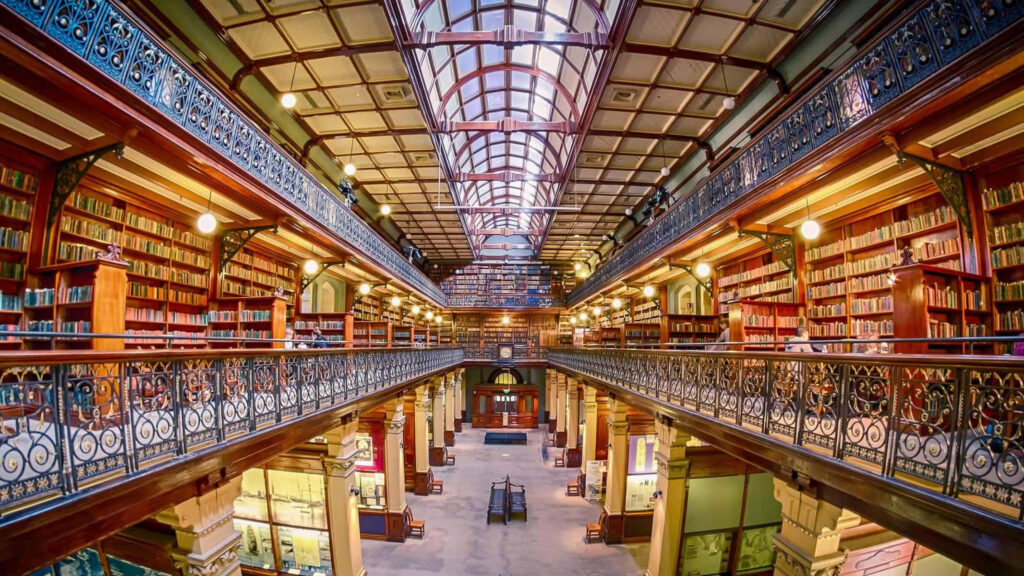 Grand interior of Adelaide State Library with ironwork arched ceilings and book-filled shelves wallpaper