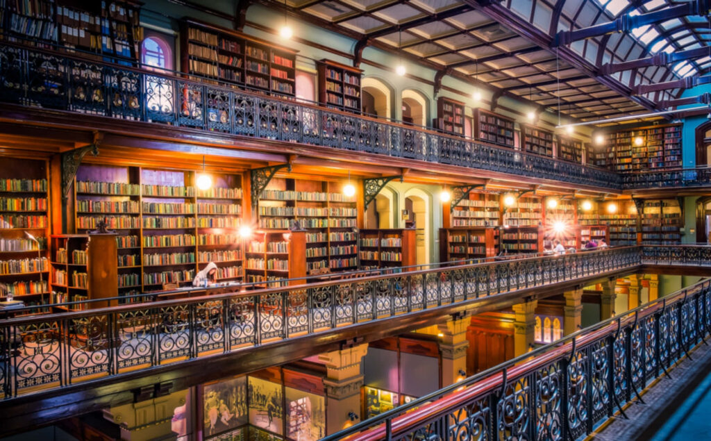 Adelaide State Library interior with ornate balconies wooden bookshelves and warm glowing lights Wallpaper