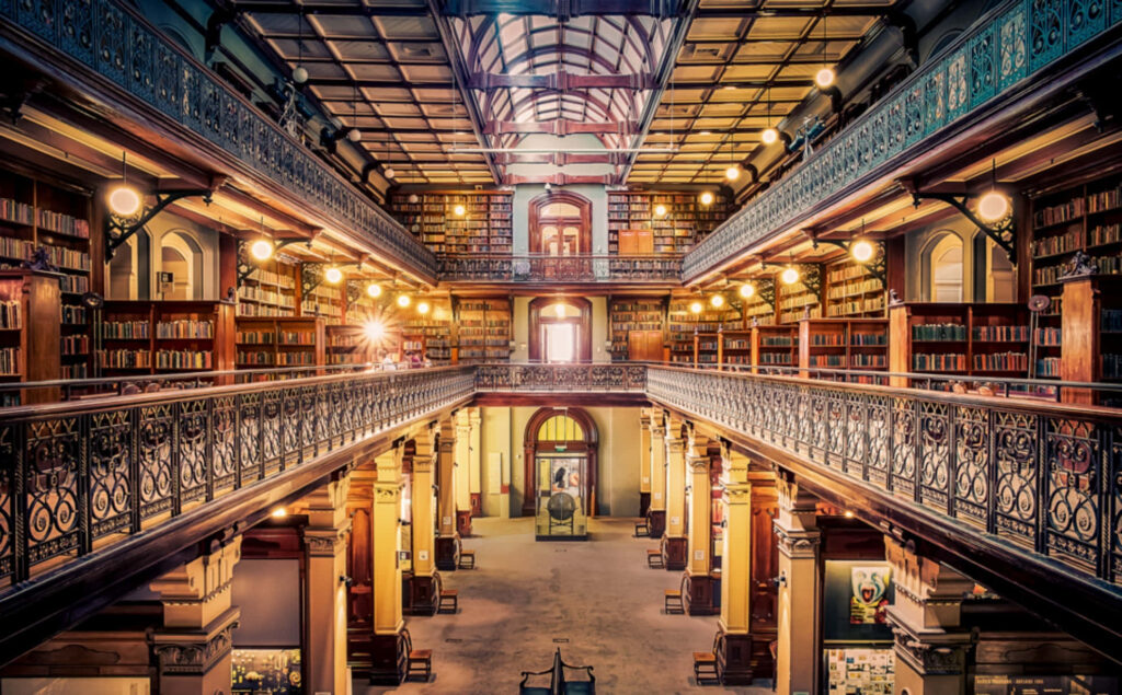 Interior view of Adelaide State Library with ornate iron railings and book-lined balconies in warm light Wallpaper