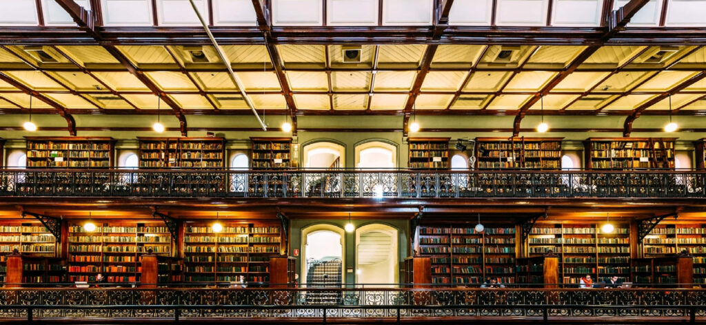 Adelaide State Library interior with towering bookshelves intricate ironwork and warm lighting Wallpaper