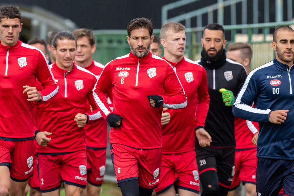 Adelaide United players training on field in red kits showing team unity and match preparation Wallpaper