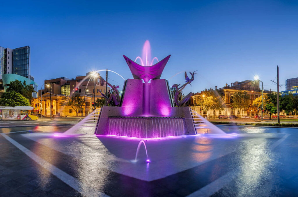 Adelaide Victoria Square Fountain at twilight with purple lights and modern city skyline background Wallpaper