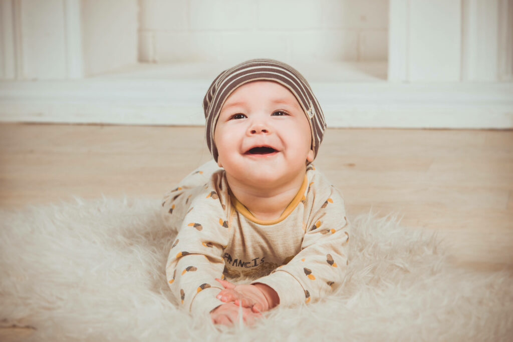 Smiling baby in cozy outfit and striped hat on soft white rug radiating warmth and innocence Wallpaper