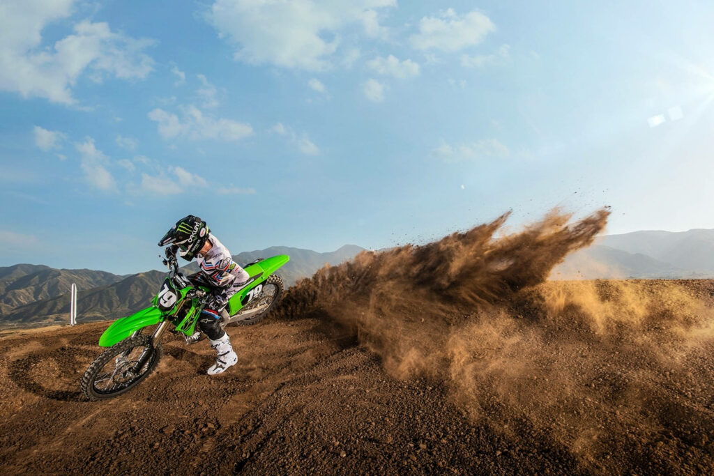 Dirt bike racing on rugged terrain with dust clouds and scenic mountain landscape background Wallpaper