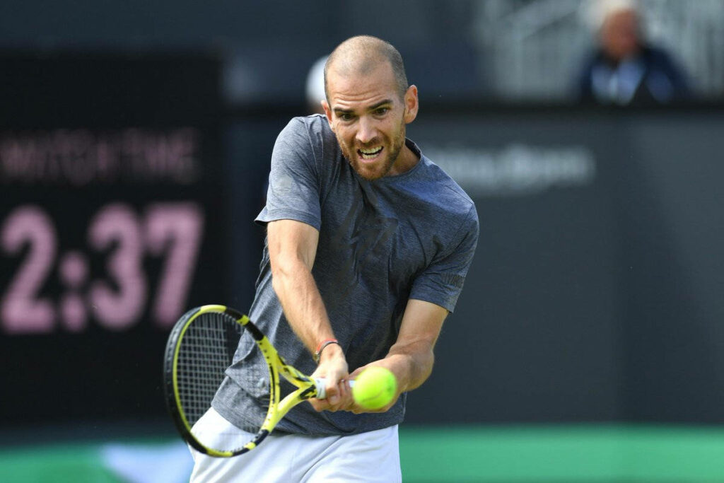 Adrian Mannarino hitting powerful backhand during intense tennis match action wallpaper background