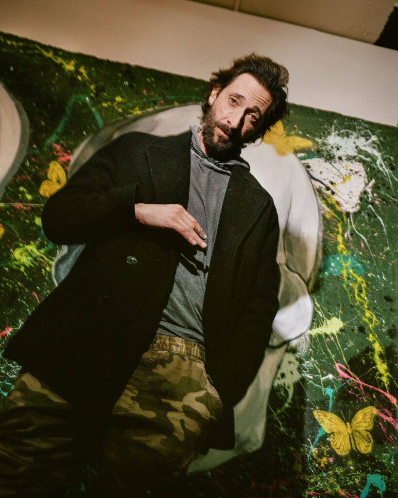 Adrien Brody in front of colorful abstract art with yellow butterflies creative wallpaper background