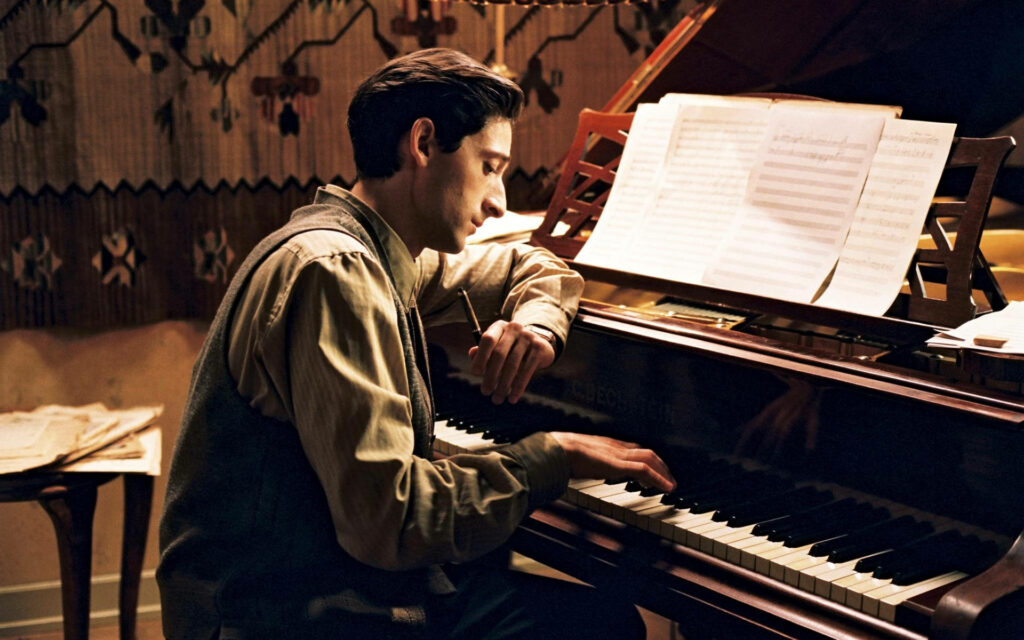 Adrien Brody intensely playing piano surrounded by sheet music in a warm softly lit room wallpaper