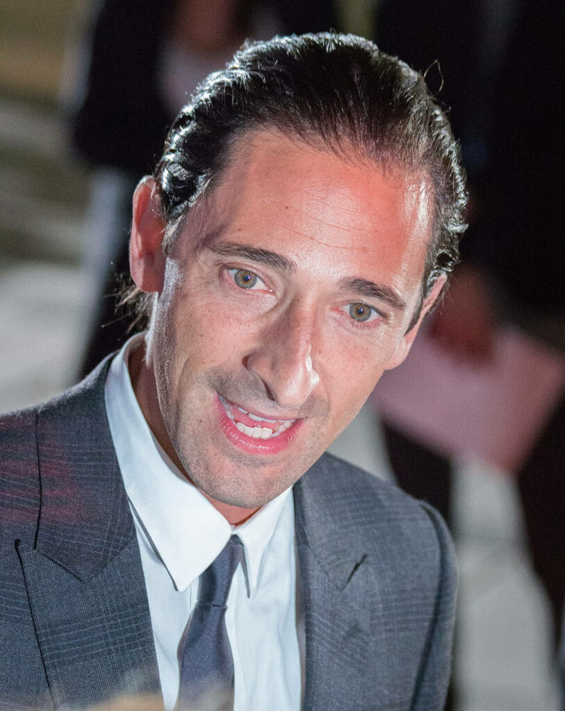 Adrien Brody in sharp suit mid-conversation with blurred background engaging wallpaper image