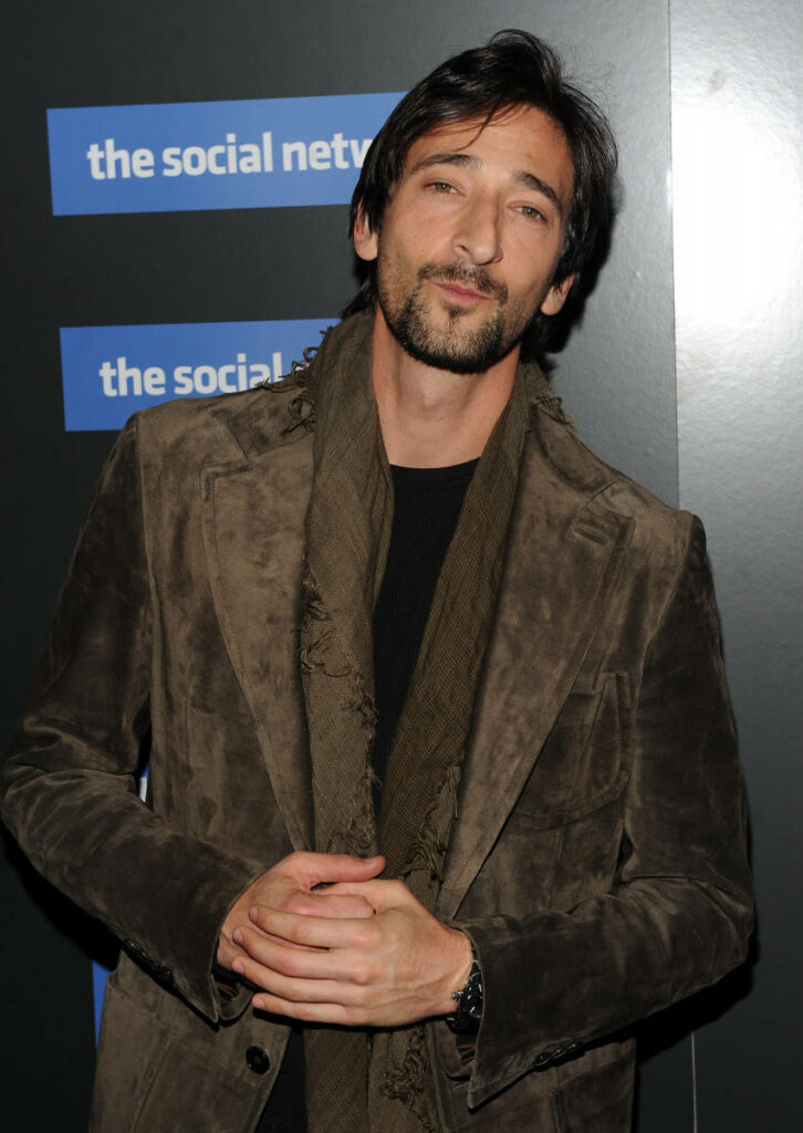 Adrien Brody stylish in brown coat modern backdrop sophisticated wallpaper background