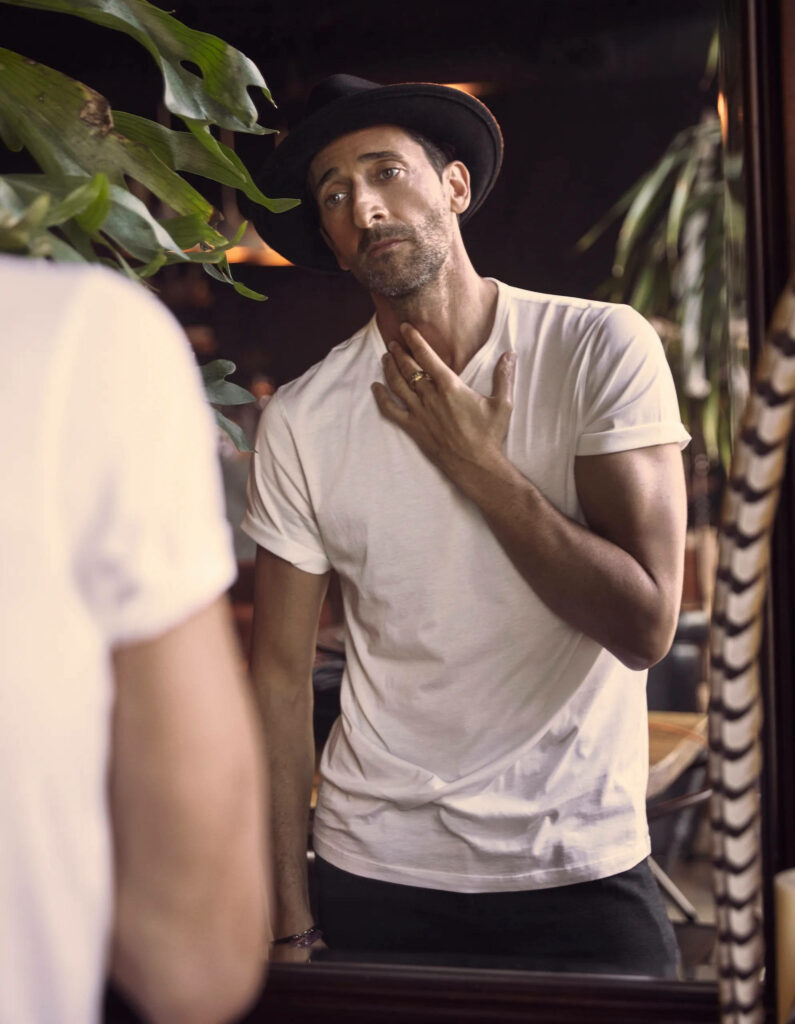 Adrien Brody in white t-shirt black hat gazing thoughtfully at mirror reflection stylish portrait Wallpaper